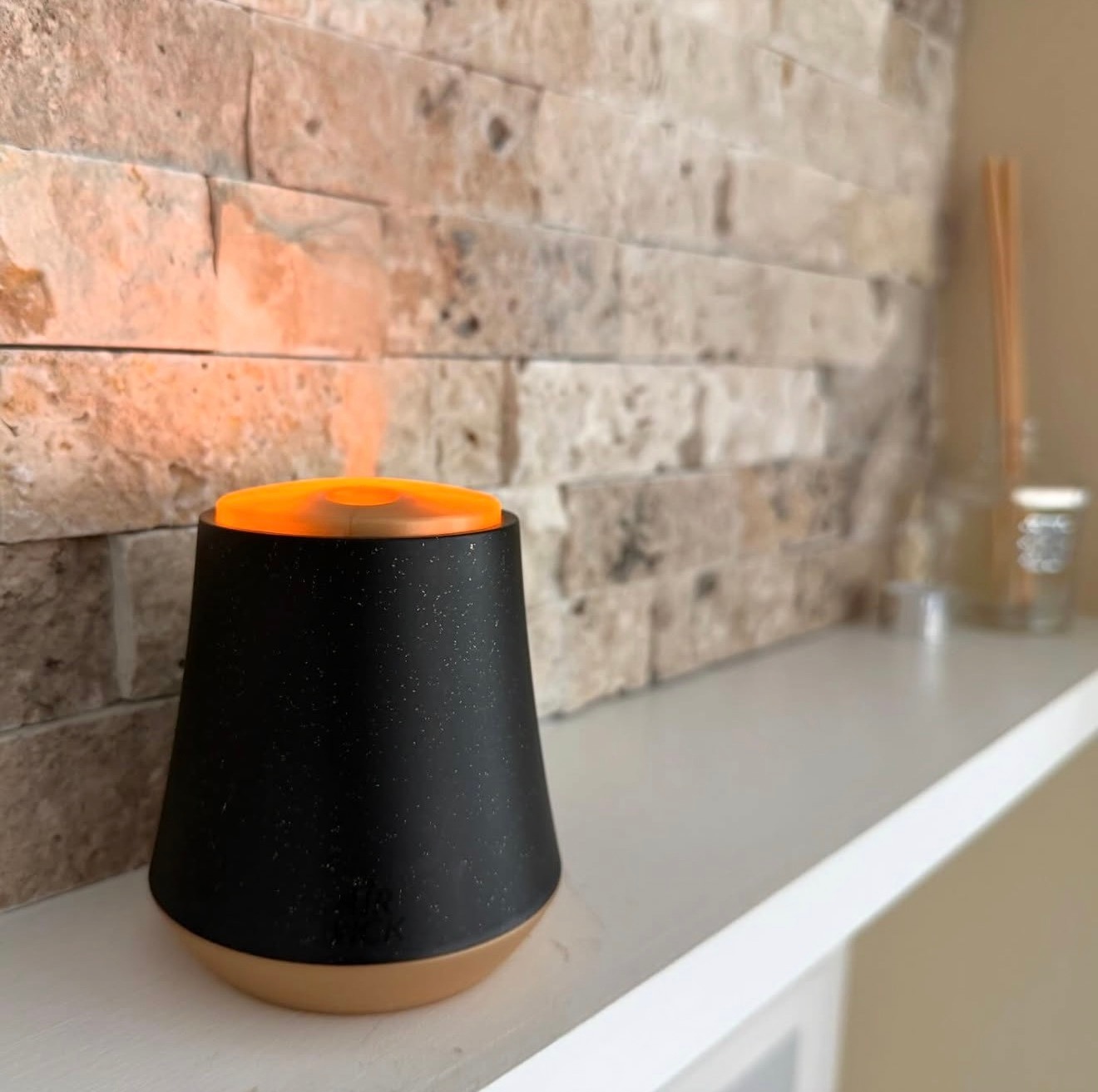 Black candle and diffuser with orange top on a stone wall shelf